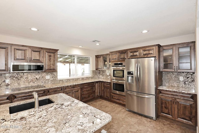 kitchen featuring appliances with stainless steel finishes, tasteful backsplash, sink, light stone countertops, and dark brown cabinets