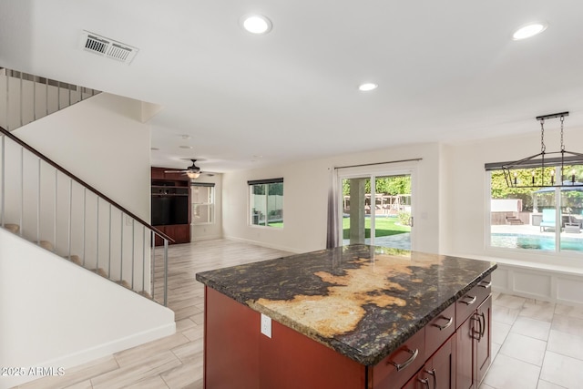 kitchen featuring decorative light fixtures, dark stone counters, ceiling fan, and a kitchen island