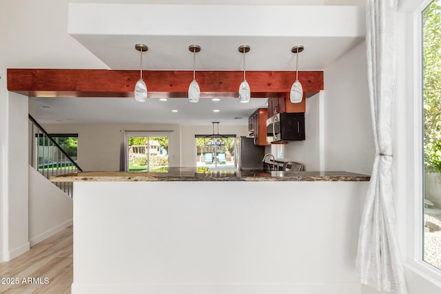 kitchen featuring pendant lighting, dark stone counters, kitchen peninsula, and beamed ceiling