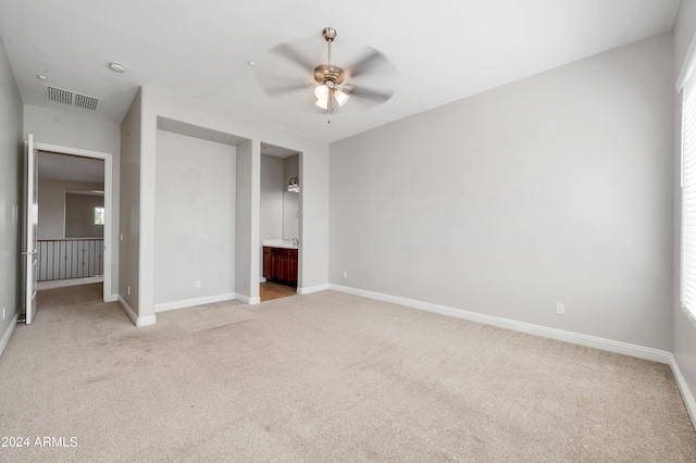 unfurnished bedroom with multiple windows, light colored carpet, ensuite bathroom, and ceiling fan