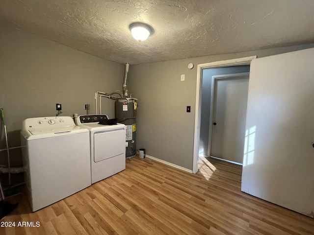 clothes washing area with water heater, washing machine and dryer, a textured ceiling, and light hardwood / wood-style floors