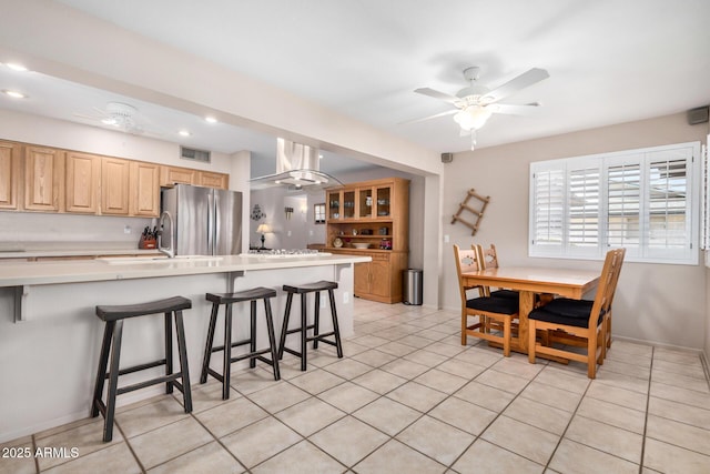 kitchen featuring visible vents, freestanding refrigerator, ceiling fan, light countertops, and a kitchen bar