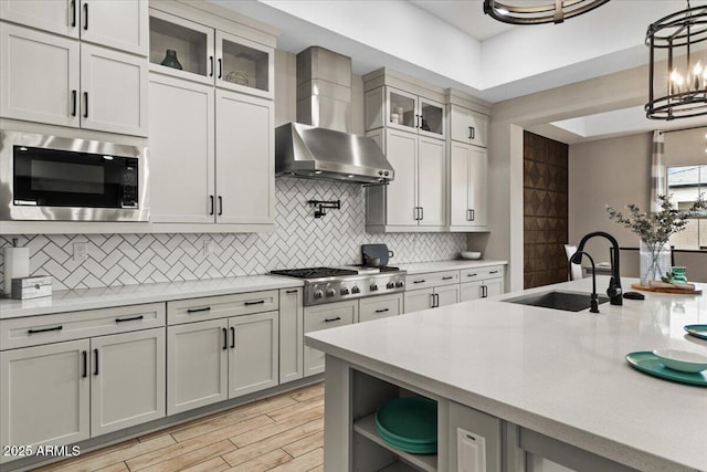 kitchen with built in microwave, wall chimney exhaust hood, sink, hanging light fixtures, and stainless steel gas stovetop