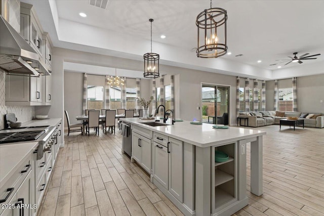 kitchen with pendant lighting, dishwasher, sink, a center island with sink, and wall chimney exhaust hood