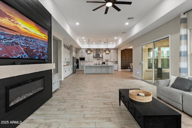 living room with ceiling fan, sink, and light wood-type flooring