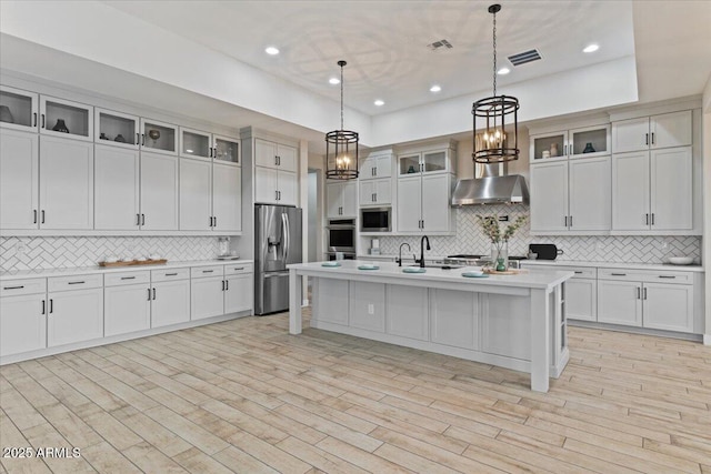 kitchen with appliances with stainless steel finishes, range hood, a kitchen bar, hanging light fixtures, and a center island with sink