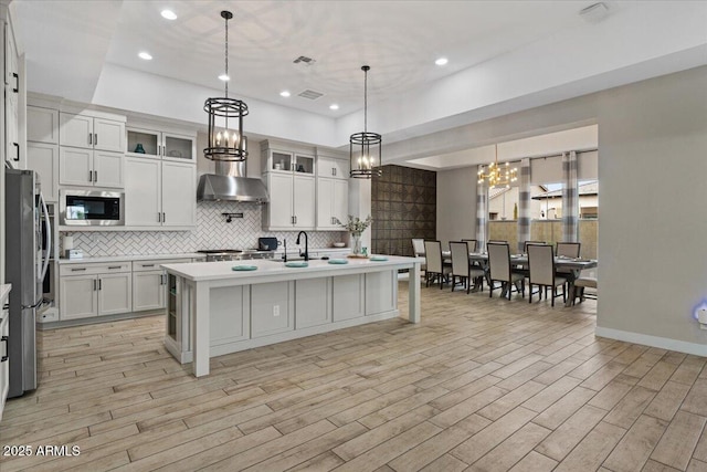 kitchen featuring light hardwood / wood-style flooring, a kitchen island with sink, hanging light fixtures, stainless steel appliances, and white cabinets