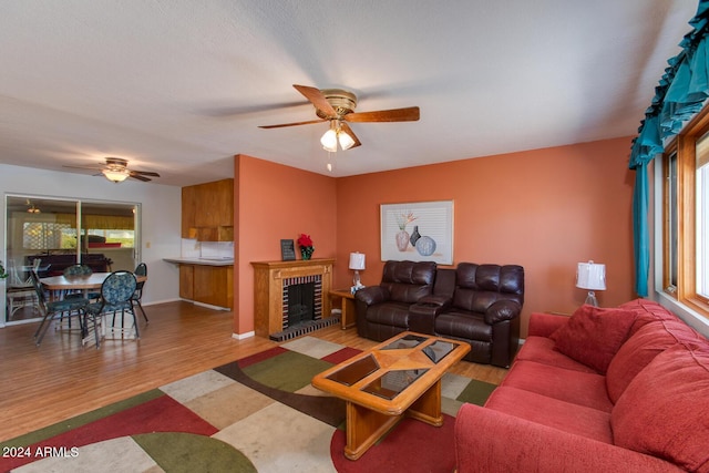 living room with a brick fireplace, ceiling fan, and light hardwood / wood-style flooring