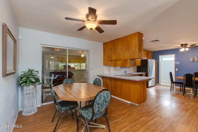 kitchen featuring kitchen peninsula, light wood-type flooring, ceiling fan, sink, and stainless steel refrigerator