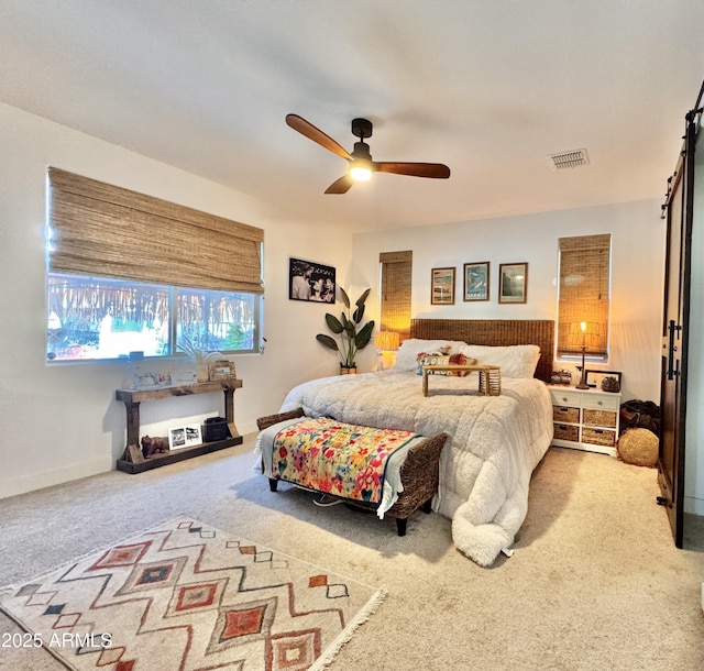 carpeted bedroom with a barn door and ceiling fan