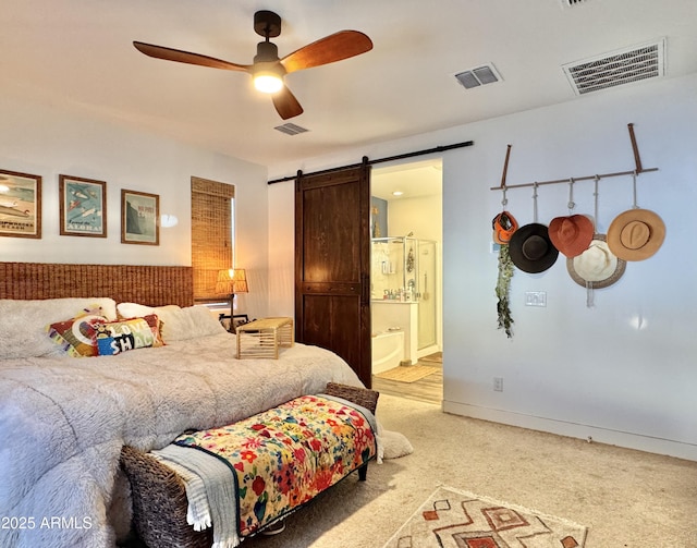 carpeted bedroom with a barn door, connected bathroom, and ceiling fan