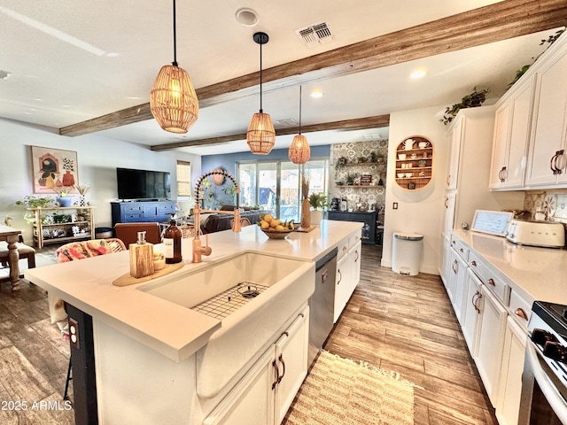 kitchen featuring hanging light fixtures, appliances with stainless steel finishes, an island with sink, beamed ceiling, and white cabinets