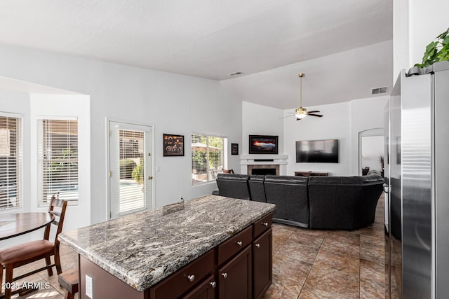 kitchen featuring dark brown cabinetry, a kitchen island, ceiling fan, vaulted ceiling, and light stone counters