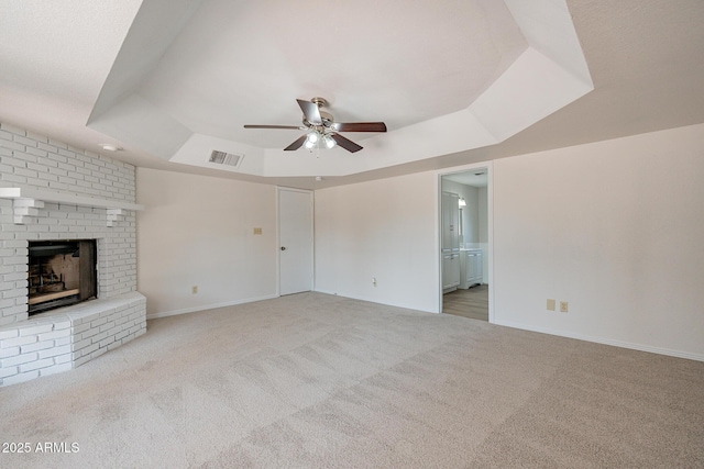 unfurnished living room featuring a raised ceiling, ceiling fan, light carpet, and a brick fireplace