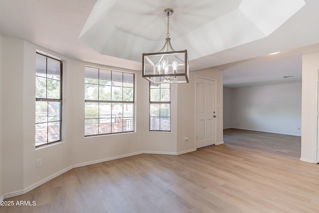 unfurnished room with an inviting chandelier, a raised ceiling, and light hardwood / wood-style floors