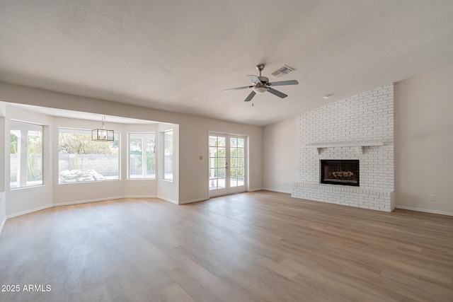 unfurnished living room featuring vaulted ceiling, a brick fireplace, ceiling fan, light wood-type flooring, and a textured ceiling