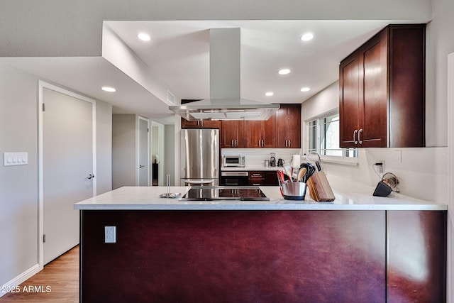 kitchen with black stovetop, freestanding refrigerator, island range hood, light wood-type flooring, and a peninsula