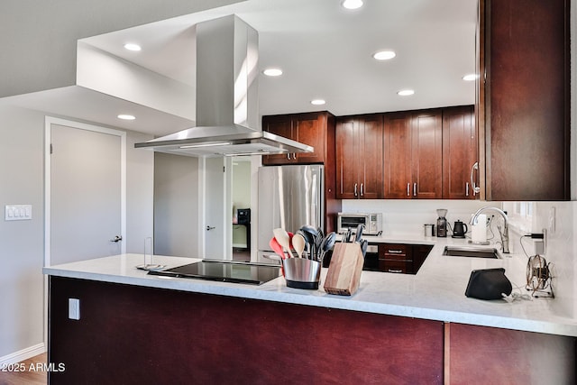 kitchen featuring freestanding refrigerator, a peninsula, island exhaust hood, black electric stovetop, and a sink