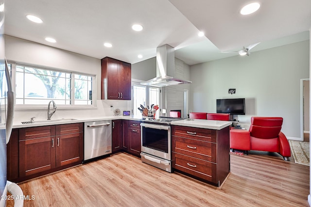 kitchen with appliances with stainless steel finishes, a sink, light wood-type flooring, a peninsula, and wall chimney exhaust hood