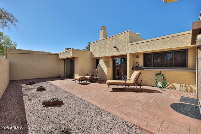 rear view of house with a chimney, a patio area, fence, and stucco siding