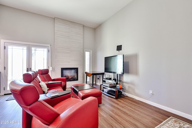 living room featuring baseboards, a tiled fireplace, wood finished floors, a high ceiling, and french doors