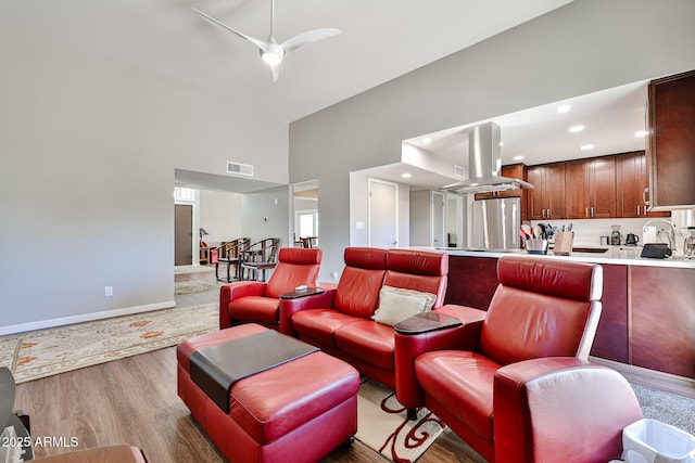 living area with visible vents, a high ceiling, light wood-style floors, ceiling fan, and baseboards