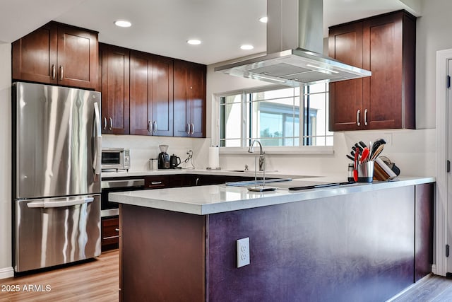 kitchen with stainless steel appliances, light countertops, dark brown cabinets, island range hood, and light wood-type flooring