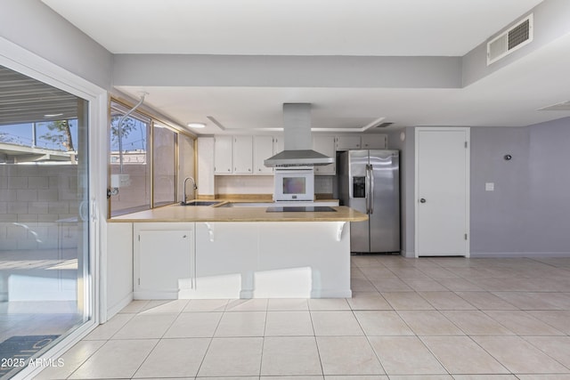 kitchen with sink, stainless steel fridge, white cabinetry, island exhaust hood, and kitchen peninsula