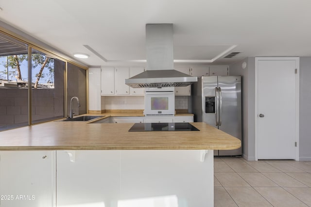 kitchen with stainless steel fridge, island range hood, kitchen peninsula, white cabinets, and oven