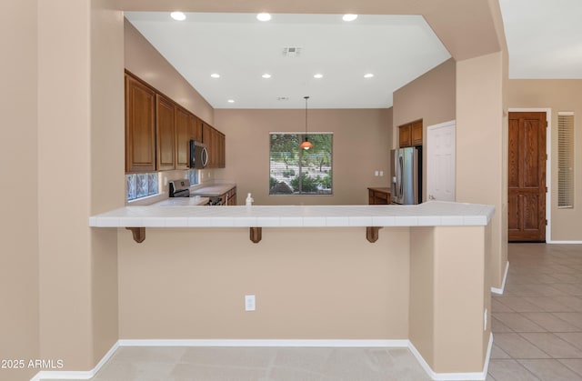 42122 N Anthem Springs Rd, Anthem, AZ 85086 - kitchen with stainless steel appliances, brown cabinets, a kitchen breakfast bar, tile counters, and recessed lighting