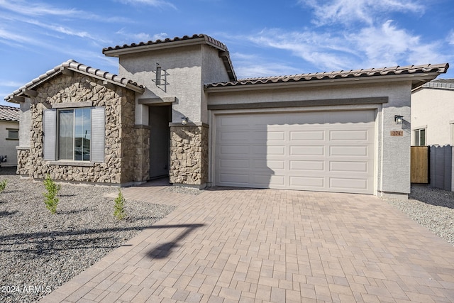 mediterranean / spanish house with a garage, fence, stone siding, decorative driveway, and stucco siding