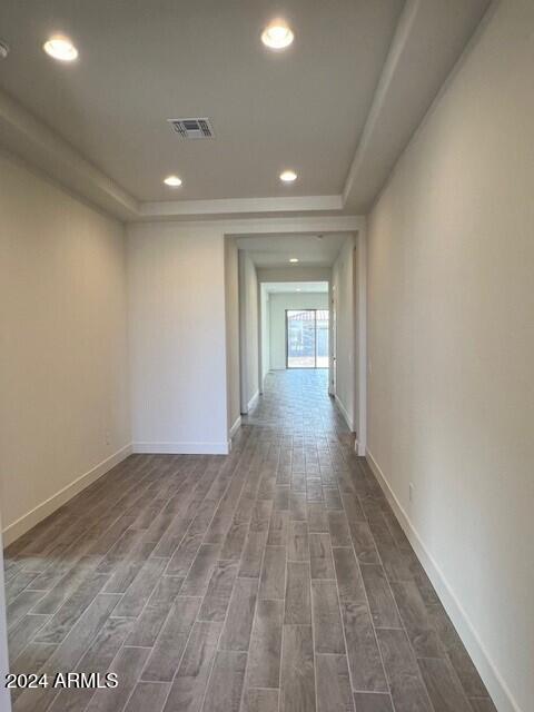 corridor with dark wood-style flooring, recessed lighting, a raised ceiling, visible vents, and baseboards