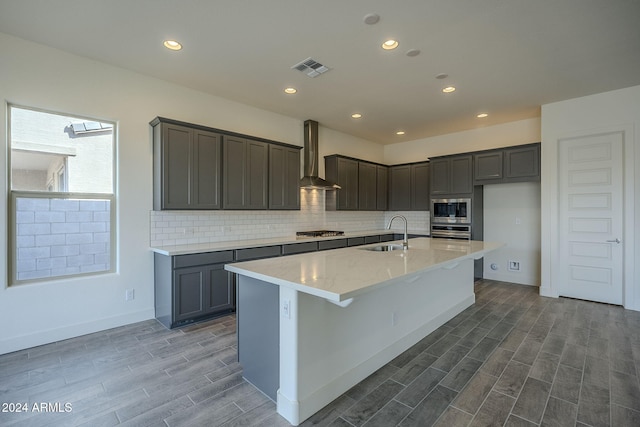 kitchen with stainless steel appliances, wood finish floors, a sink, visible vents, and wall chimney range hood