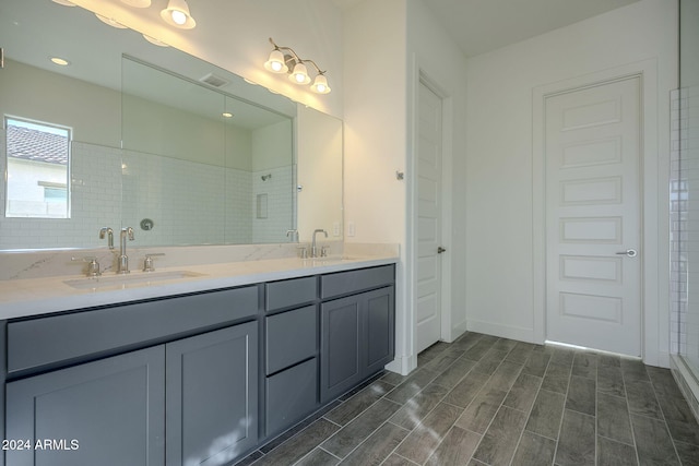 bathroom with wood finish floors, a sink, visible vents, a tile shower, and double vanity