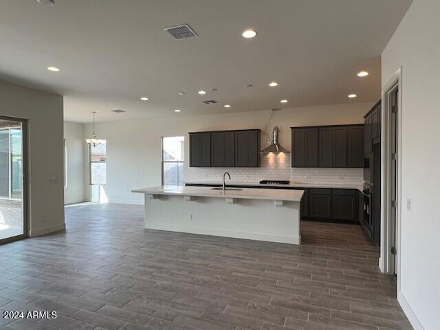 kitchen with a center island with sink, a wealth of natural light, wall chimney exhaust hood, and dark hardwood / wood-style floors