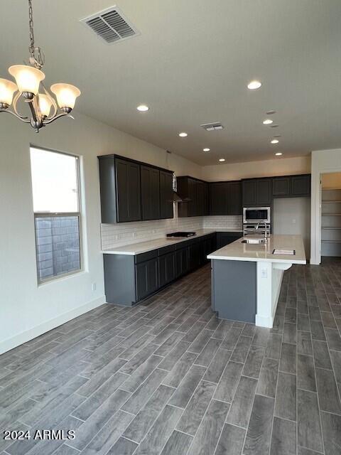 kitchen with decorative backsplash, appliances with stainless steel finishes, dark wood-type flooring, pendant lighting, and an island with sink