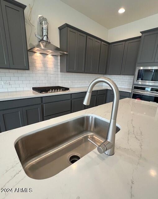 kitchen featuring recessed lighting, a sink, appliances with stainless steel finishes, backsplash, and light stone countertops