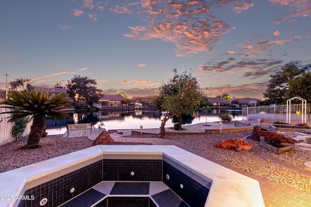 patio terrace at dusk featuring a water view and fence