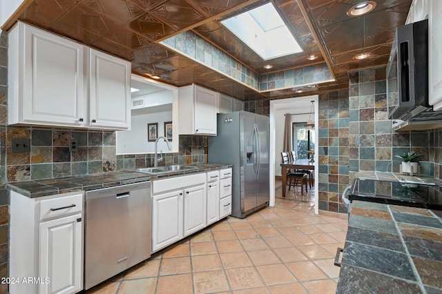 kitchen featuring a skylight, sink, stainless steel appliances, tasteful backsplash, and white cabinets