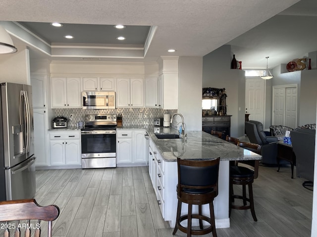 kitchen with sink, a tray ceiling, appliances with stainless steel finishes, a kitchen breakfast bar, and white cabinets