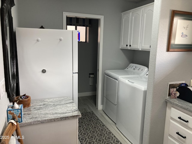 clothes washing area featuring light wood-type flooring, cabinets, and washer and clothes dryer