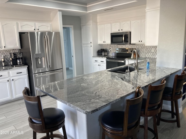 kitchen featuring white cabinets, a breakfast bar, kitchen peninsula, and appliances with stainless steel finishes