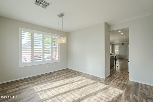 empty room with wood finished floors, visible vents, and baseboards