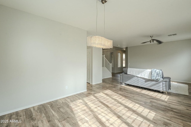 empty room with stairs, wood finished floors, visible vents, and baseboards