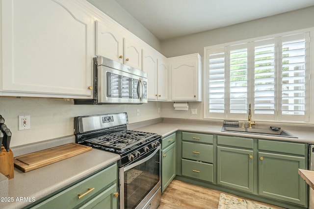 kitchen featuring a sink, stainless steel appliances, green cabinets, white cabinets, and light wood finished floors