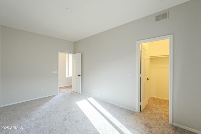 unfurnished bedroom featuring a walk in closet, baseboards, visible vents, and light carpet