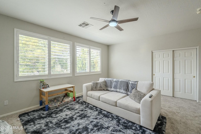 carpeted living room with a wealth of natural light, visible vents, baseboards, and a ceiling fan