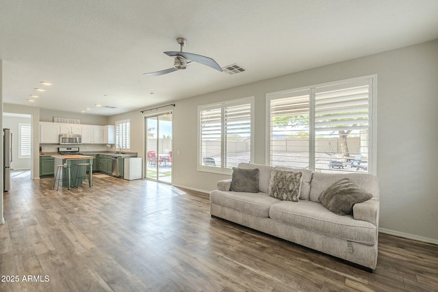 living room featuring visible vents, baseboards, wood finished floors, and a ceiling fan