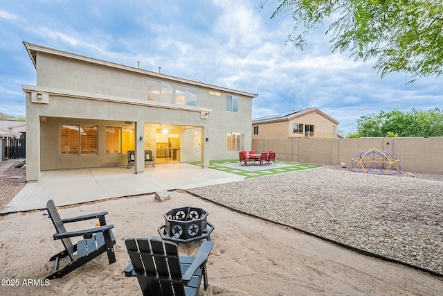 rear view of house with a patio, stucco siding, a fenced backyard, and an outdoor fire pit