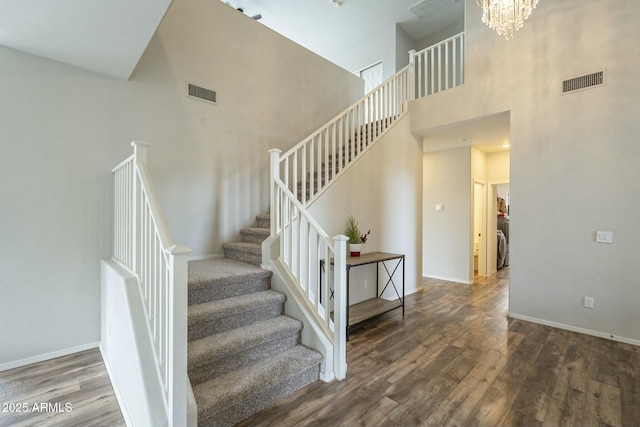 staircase with visible vents, baseboards, wood finished floors, and a towering ceiling